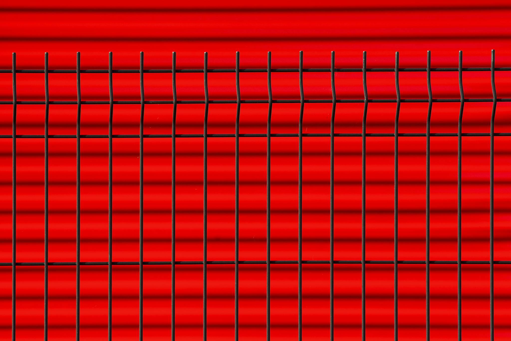 Close-up of a black metal fence against a vibrant red background, creating geometric patterns.