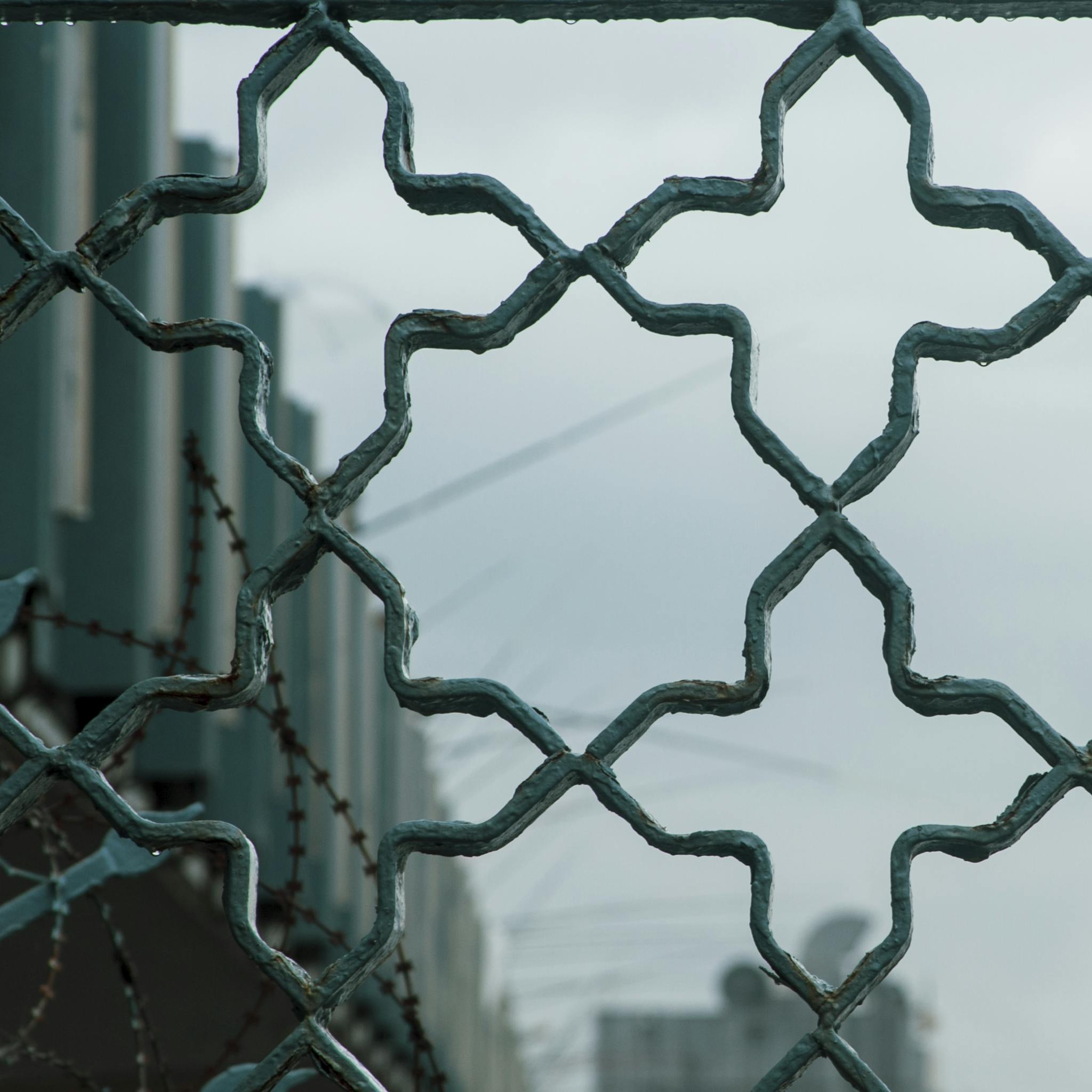 Close-up of a metal fence with a geometric pattern and barbed wire in an urban setting.