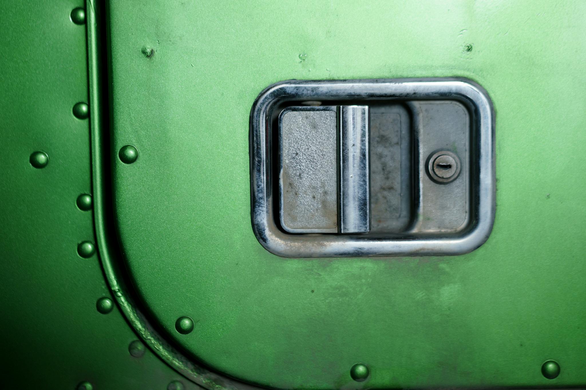 Detailed close-up of a metallic door handle with keyhole on green metal surface.